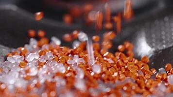Macro frame of white and orange plastic granules. The polymer composite is poured into a tank for further production and casting in special molds. Production video