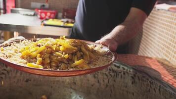 The chef puts carrots with a slotted spoon in a plate with rice from a large cauldron for pilaf video
