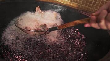 The chef puts pieces of meat with a slotted spoon into the oil boiling in a large pilaf cauldron video