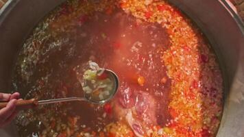 Chef mixes meat soup with vegetables in a large cauldron with a slotted spoon video