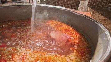 Chef mixes meat soup with vegetables in a large cauldron with a slotted spoon video