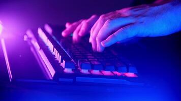 Close-up shot of a male hacker's hands typing on a dark keyboard in a neon light. video
