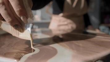Brown paint flows out of the cup and onto the surface of the painting, creating distinctive wavy lines. Close up. Slow motion video