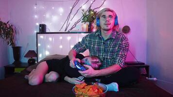 Young man is playing a game on a console, with headphones on, while his girlfriend sleeps on his lap. video