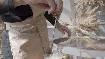 An artist, wearing an apron, carefully corrects the edges of a painting and brings them to perfection by removing any streaks of paint. Close up. Slow motion video
