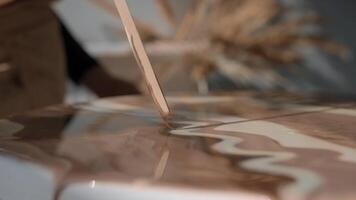 Artist paints a picture using epoxy resin and a wooden stick from which it flows onto the canvas. Close up. Slow motion video