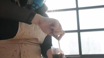 Woman is wearing a respirator as she stirs epoxy resin in a plastic cup. She is mixing paints for her upcoming painting. Close up. Slow motion video