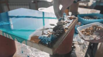 Craftswoman creates a one-of-a-kind piece of furniture using shells and pebbles as materials. She combines these natural elements to create a stunning artwork that depicts the sea and sandy shore in all its beauty. Close up. Slow motion video