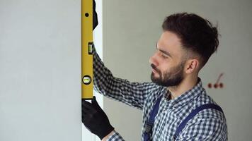 Young engineer builder measures of the vertical deviation of the wall. Bubble level ruler close up view, measuring and leveling concept video