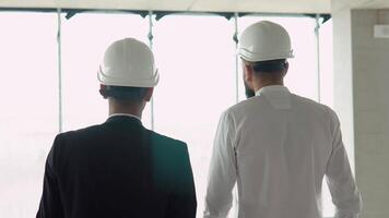 dois multiétnico construtores engenheiros trabalhadores dentro capacetes caminhando em construção às luz solar pesquisa urbano encontro arranha-céu. construtor arquiteto contratante inspetor construção capacete video