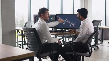 Two multiracial investors brokers analysing indexes online cryptocurrency stock. Diverse managers traders analysts discussing financial growth market at desk with pc graphs on screen video