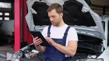 Professional car mechanic working in auto repair service with tablet. Automotive mechanical technician using laptop computer programming and investing by car diagnostic software video