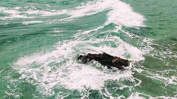 Solitude. A Solitary Rock Amidst the Turquoise Waves A lone rock stands strong in the middle of the vast ocean as turquoise waves crash around it, creating a captivating and serene scene. video