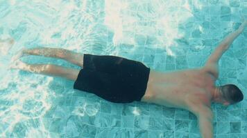 man in black shorts swims underwater in a pool, captured from an overhead viewpoint.slow motion video