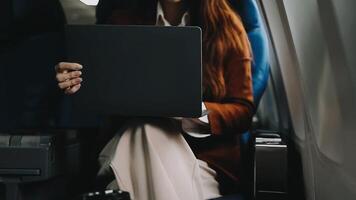 A successful asian businesswoman or female entrepreneur in formal suit in a plane sits in a business class seat and uses a documents with computer laptop during flight video