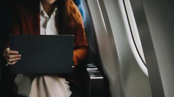 A successful asian businesswoman or female entrepreneur in formal suit in a plane sits in a business class seat and uses a documents with computer laptop during flight video