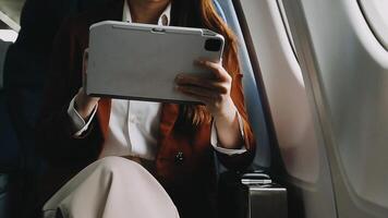 A successful asian businesswoman or female entrepreneur in formal suit in a plane sits in a business class seat and uses a documents with computer laptop during flight video