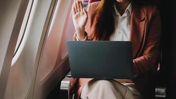 A successful asian businesswoman or female entrepreneur in formal suit in a plane sits in a business class seat and uses a documents with computer laptop during flight video