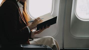 A successful asian businesswoman or female entrepreneur in formal suit in a plane sits in a business class seat and uses a documents with computer laptop during flight video