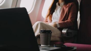 A successful asian businesswoman or female entrepreneur in formal suit in a plane sits in a business class seat and uses a documents with computer laptop during flight video