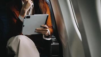 A successful asian businesswoman or female entrepreneur in formal suit in a plane sits in a business class seat and uses a documents with computer laptop during flight video