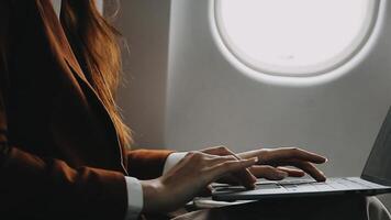 A successful asian businesswoman or female entrepreneur in formal suit in a plane sits in a business class seat and uses a documents with computer laptop during flight video