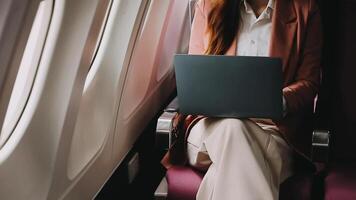 A successful asian businesswoman or female entrepreneur in formal suit in a plane sits in a business class seat and uses a documents with computer laptop during flight video