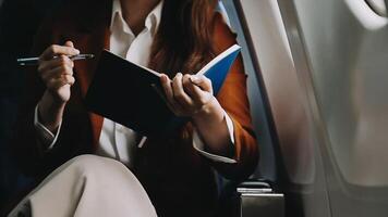 A successful asian businesswoman or female entrepreneur in formal suit in a plane sits in a business class seat and uses a documents with computer laptop during flight video