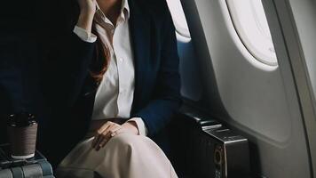 Young Asian woman uses mobile phone to check news information Sitting near the window in business class, airplane class during flight, travel and business concept video