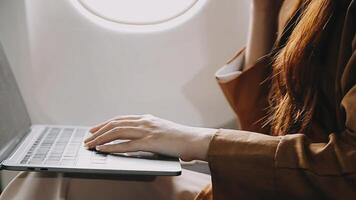 A successful asian businesswoman or female entrepreneur in formal suit in a plane sits in a business class seat and uses a documents with computer laptop during flight video