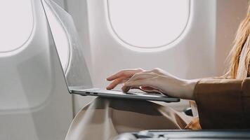 A successful asian businesswoman or female entrepreneur in formal suit in a plane sits in a business class seat and uses a documents with computer laptop during flight video