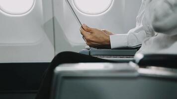 Two businessman passengers sitting in airplane cabin and working on laptop together. Businessman in brown suit showing project on notebook to businessman with eyeglasses. Business and travel concept. video