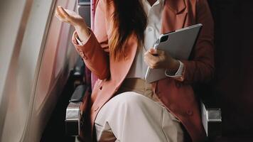 A successful asian businesswoman or female entrepreneur in formal suit in a plane sits in a business class seat and uses a documents with computer laptop during flight video