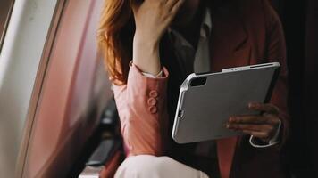 A successful asian businesswoman or female entrepreneur in formal suit in a plane sits in a business class seat and uses a documents with computer laptop during flight video