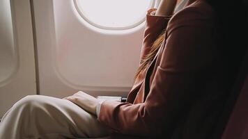 Young Asian woman uses mobile phone to check news information Sitting near the window in business class, airplane class during flight, travel and business concept video