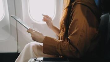 A successful asian businesswoman or female entrepreneur in formal suit in a plane sits in a business class seat and uses a documents with computer laptop during flight video