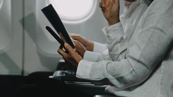 Two businessman passengers sitting in airplane cabin and working on laptop together. Businessman in brown suit showing project on notebook to businessman with eyeglasses. Business and travel concept. video