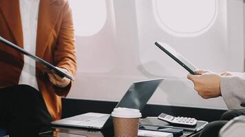 Two businessman passengers sitting in airplane cabin and working on laptop together. Businessman in brown suit showing project on notebook to businessman with eyeglasses. Business and travel concept. video