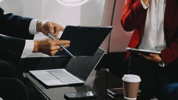 Two businessman passengers sitting in airplane cabin and working on laptop together. Businessman in brown suit showing project on notebook to businessman with eyeglasses. Business and travel concept. video