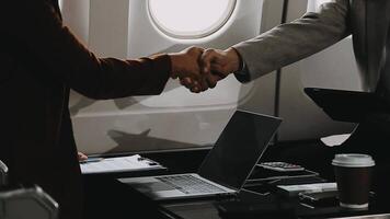 Two businessman passengers sitting in airplane cabin and working on laptop together. Businessman in brown suit showing project on notebook to businessman with eyeglasses. Business and travel concept. video
