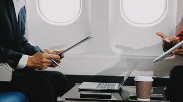 Two businessman passengers sitting in airplane cabin and working on laptop together. Businessman in brown suit showing project on notebook to businessman with eyeglasses. Business and travel concept. video