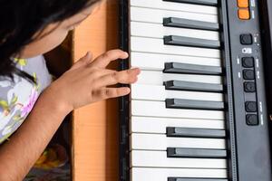 Asian cute girl playing the synthesizer or piano. Cute little kid learning how to play piano. Child's hands on the keyboard indoor. photo