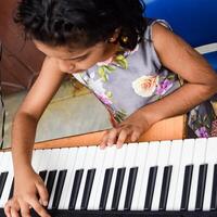 Asian cute girl playing the synthesizer or piano. Cute little kid learning how to play piano. Child's hands on the keyboard indoor. photo