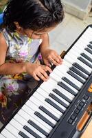 Asian cute girl playing the synthesizer or piano. Cute little kid learning how to play piano. Child's hands on the keyboard indoor. photo