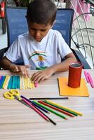 Smart Indian little boy performing best out of waste activity with different colourful objects during the summer vacations, Cute Indian Kid doing best our of waste activity at home on wooden table photo