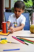 Smart Indian little boy performing best out of waste activity with different colourful objects during the summer vacations, Cute Indian Kid doing best our of waste activity at home on wooden table photo
