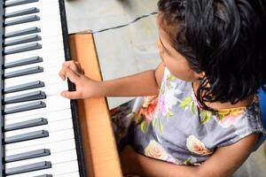 Asian cute girl playing the synthesizer or piano. Cute little kid learning how to play piano. Child's hands on the keyboard indoor. photo