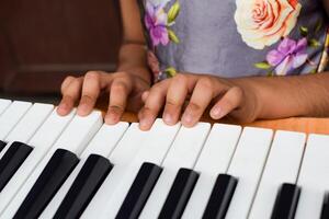 Asian cute girl playing the synthesizer or piano. Cute little kid learning how to play piano. Child's hands on the keyboard indoor. photo