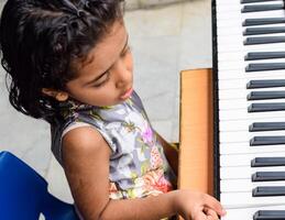 Asian cute girl playing the synthesizer or piano. Cute little kid learning how to play piano. Child's hands on the keyboard indoor. photo