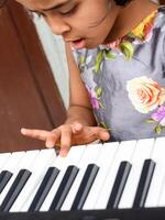 Asian cute girl playing the synthesizer or piano. Cute little kid learning how to play piano. Child's hands on the keyboard indoor. photo
